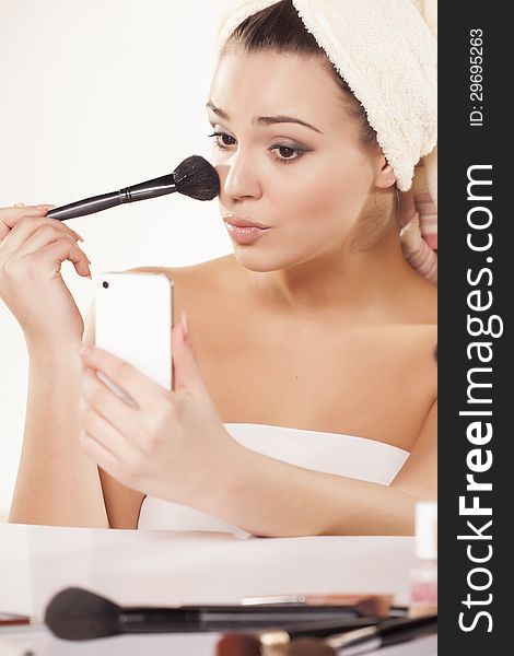 Girl with towel on head fixes her makeup and uses her smartphone as a mirror