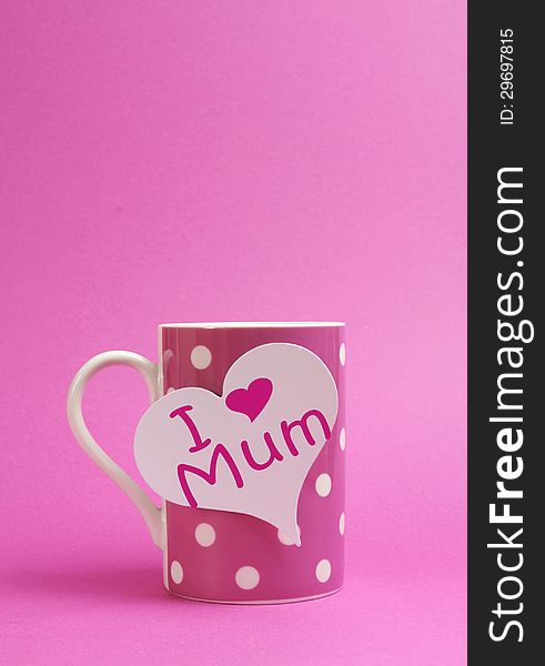 Pink polka dot coffee or tea mug with heart shape white gift tag with I Heart Love Mum for Mothers Day on pink background with copy space for your text here. Pink polka dot coffee or tea mug with heart shape white gift tag with I Heart Love Mum for Mothers Day on pink background with copy space for your text here.