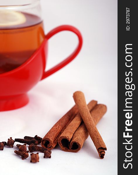 Cinnamon and cloves in front of a red cup of tea. Cinnamon and cloves in front of a red cup of tea