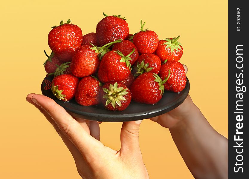 Black plate with a strawberry in female hands. Black plate with a strawberry in female hands.