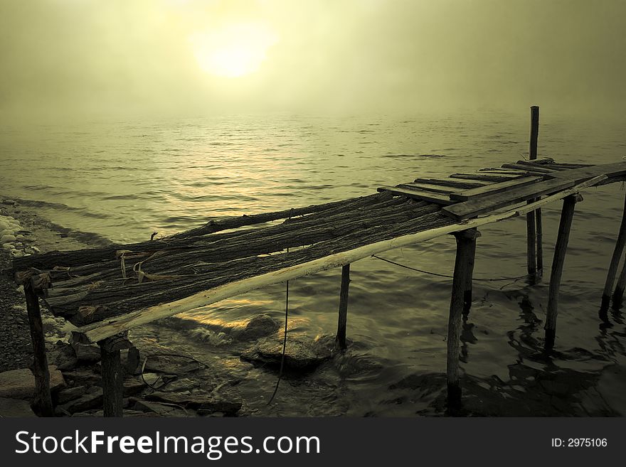 Wooden old bridge on a sunrise background. Beautiful water idyllic scen in cold  vintage-green colors.