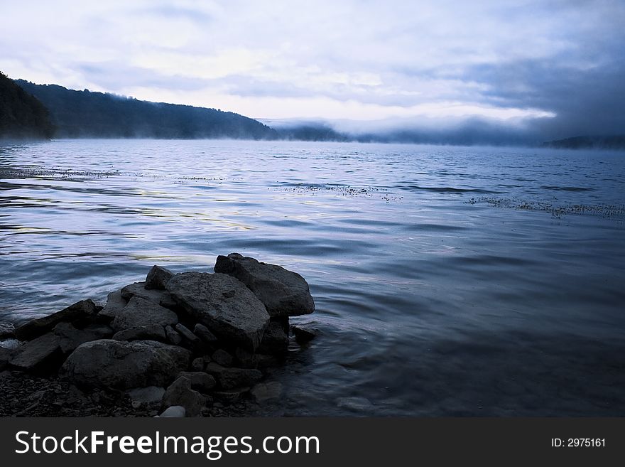 Beautiful water landscape with a fog above water & stones on a foreground. Image in blue, cold tone. Beautiful water landscape with a fog above water & stones on a foreground. Image in blue, cold tone.