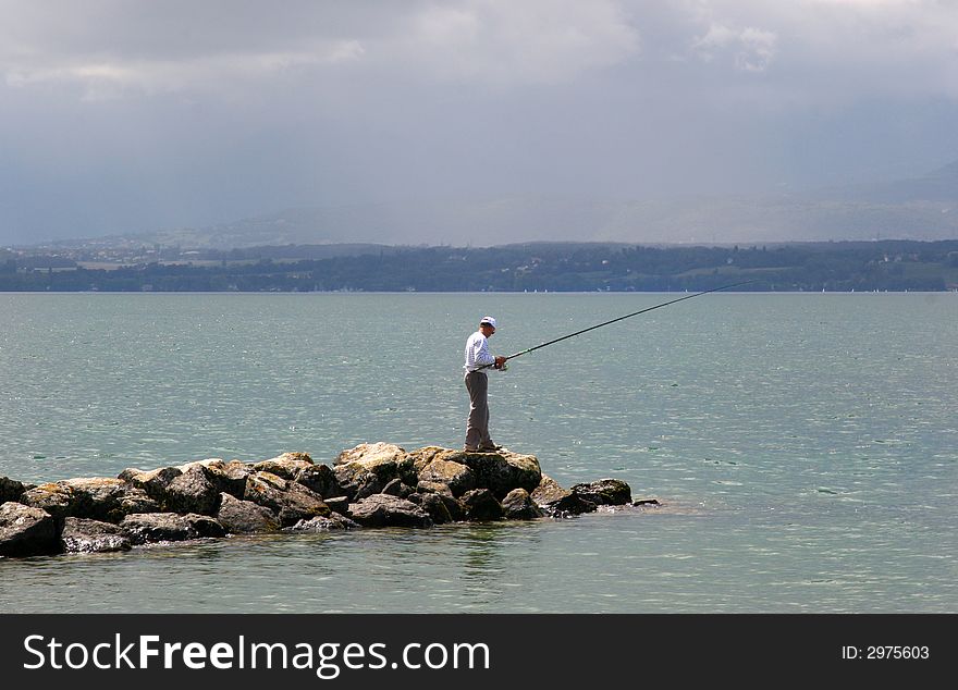 Fisherman at edge of rock peir on a lake