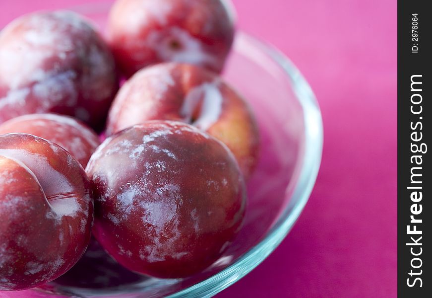 Bowl of plums on pink background