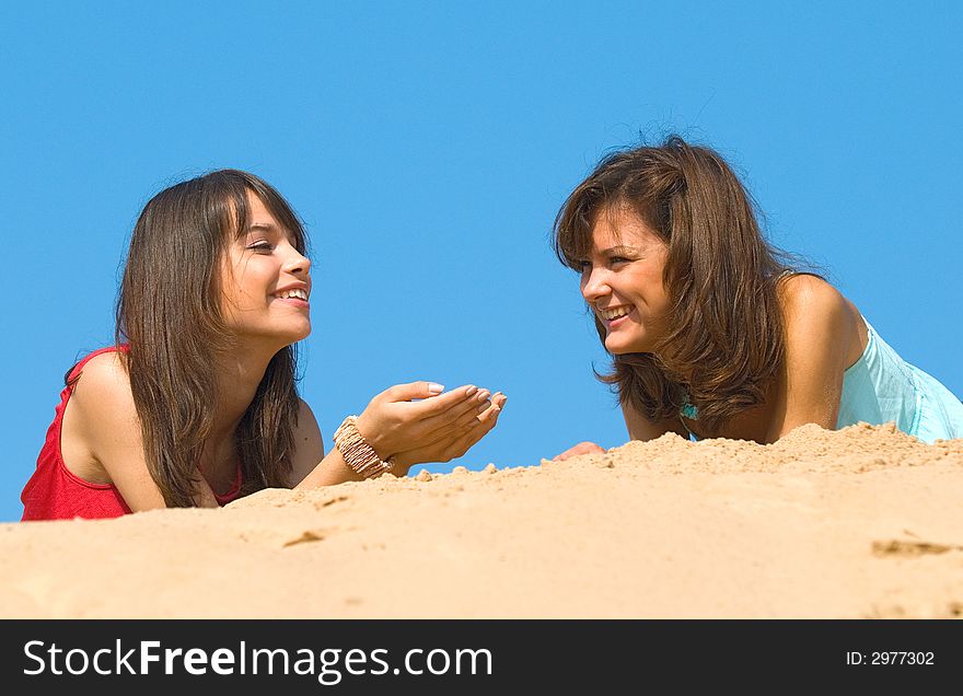 Two happy girlfriends talk on sand under the sun