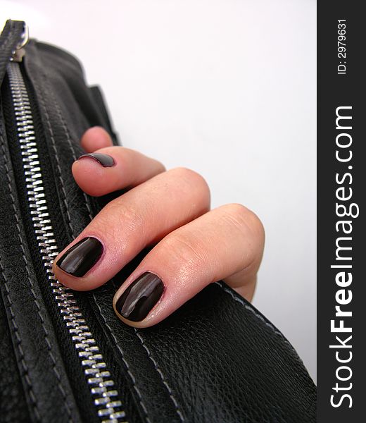 Woman's hand holding a leather handbag. Dark fingernails.