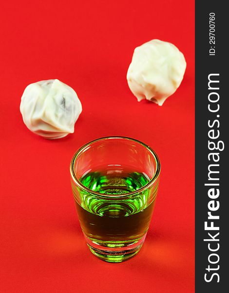 Glass with green liquor and white chocolate on a red background. Glass with green liquor and white chocolate on a red background