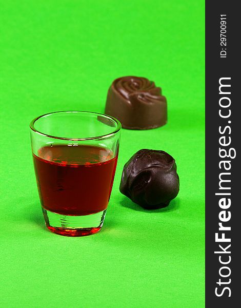 Glass with red liqueur and dark chocolate on a green background. Glass with red liqueur and dark chocolate on a green background