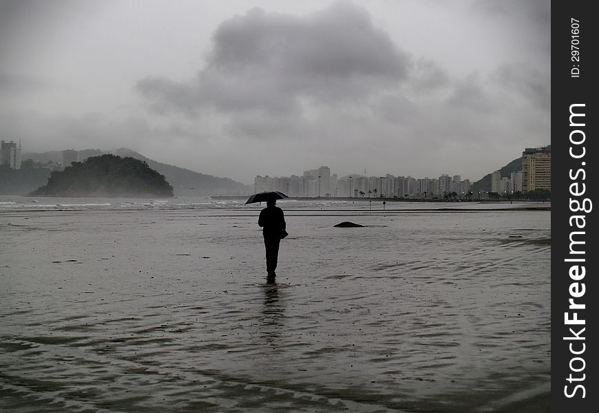 A man walking at the beach of Santos during a rainy day. A man walking at the beach of Santos during a rainy day