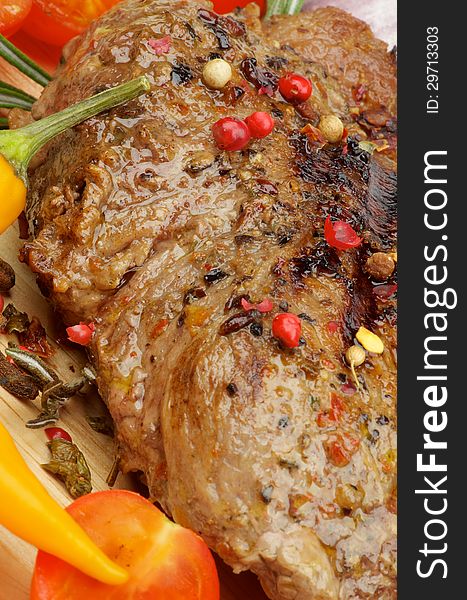 Roasted Beef with Spices, Peppercorns and Herbs closeup on Wooden Board with Vegetables