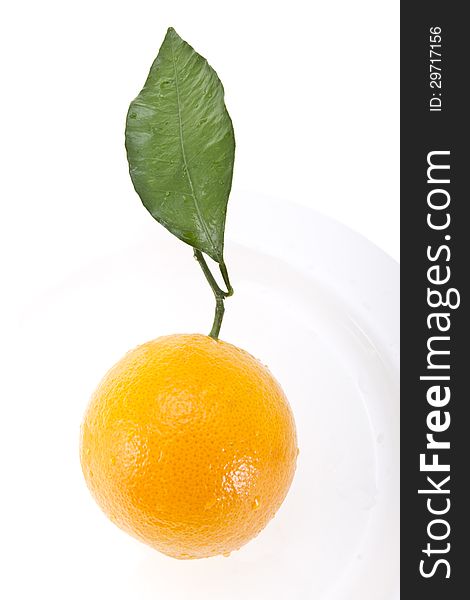 Ripe orange with a green leaf inside of a white plate isolated on white.