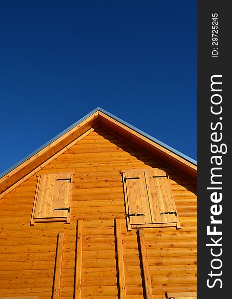 Detail of wooden house - wall, windows and roof against blue sky