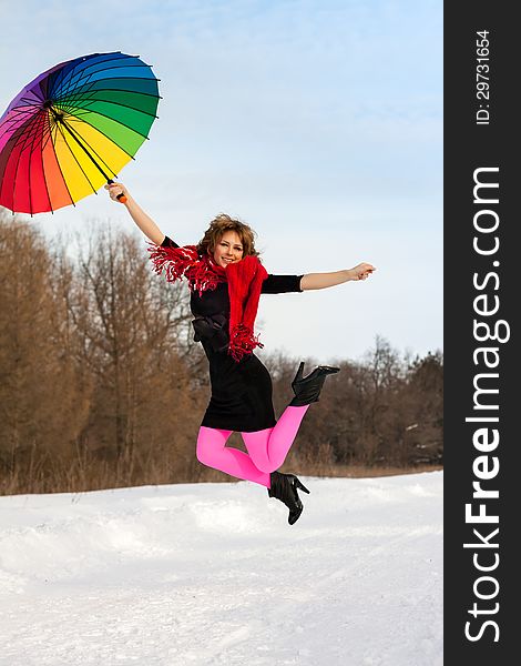 Young blond beautiful woman jumping against wood in bright scarf with color umbrella in winter. Young blond beautiful woman jumping against wood in bright scarf with color umbrella in winter