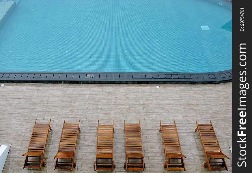 Wooden deckchairs around a swimming pool. Wooden deckchairs around a swimming pool