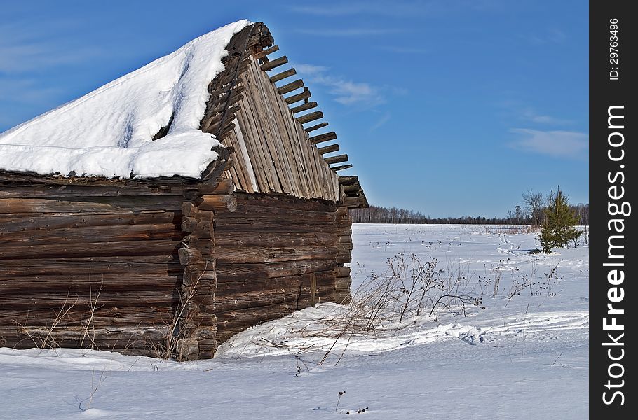 Country view and old wooden barn with a snow-covered sagging roof, winter sunny day. Country view and old wooden barn with a snow-covered sagging roof, winter sunny day