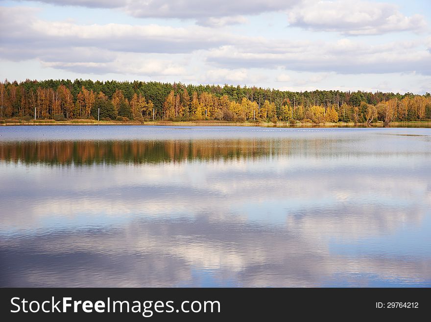 Autumn landscape with lake, forest and clouds sky