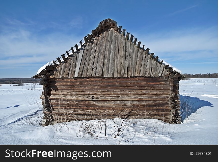 Old wooden barn on a snowy field, winter sunny day