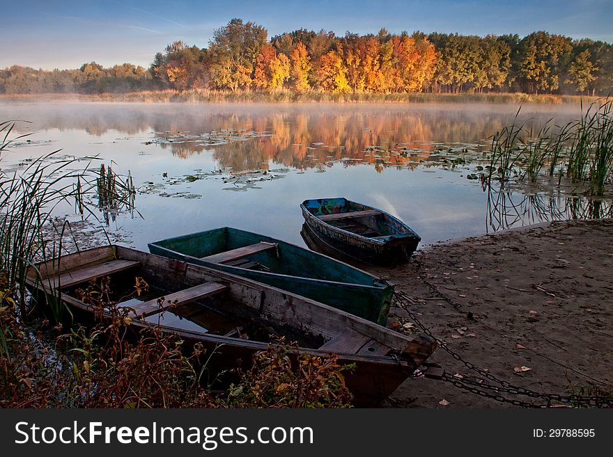 Boats on the quiet autumn lake, yellow forest, calm water