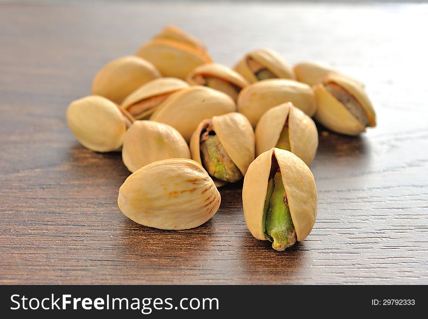 Roasted salted pistachios are a small pile on brown wooden table. Roasted salted pistachios are a small pile on brown wooden table