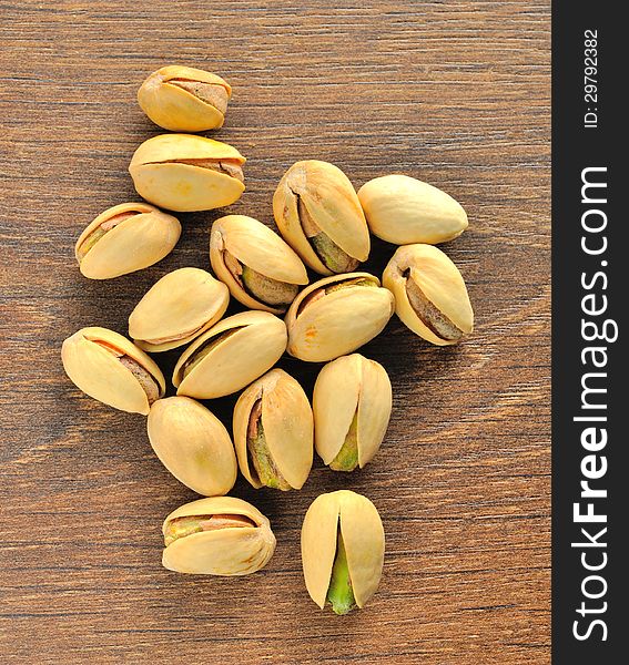 Roasted salted pistachios are a small pile on brown wooden table