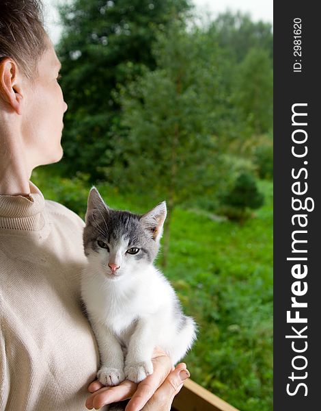 Woman with little kitten in hands is standing near a window and loking at view. Woman with little kitten in hands is standing near a window and loking at view