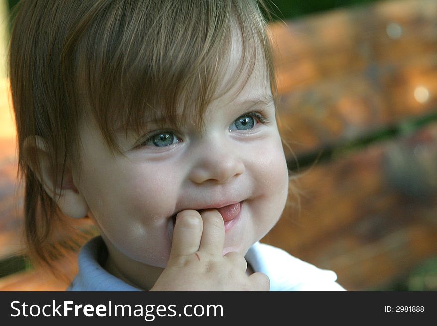 Little smiling girl outdoors with fingers in the mouth