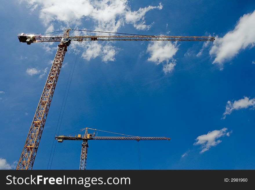 Two idle cranes standing close standing against a blue cloudy sky