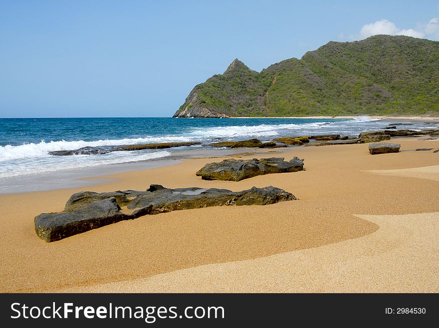 Whitewash on tropical caribbean island with hill on the horizon and rocks on the beach. Whitewash on tropical caribbean island with hill on the horizon and rocks on the beach