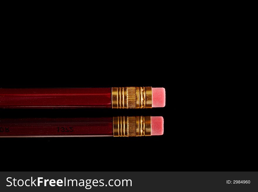Red pencil with eraser on mirror over black background. Red pencil with eraser on mirror over black background