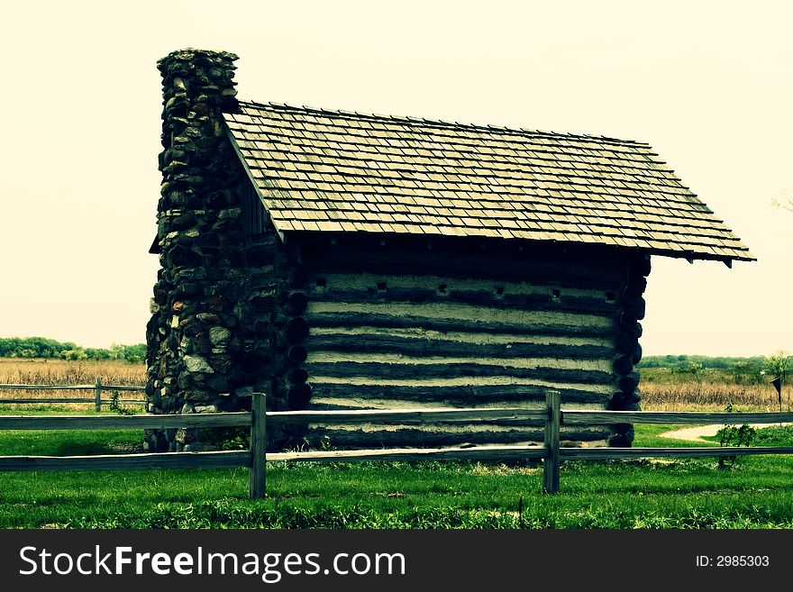 Old log cabin surrounded by wooden fence, cross-processed