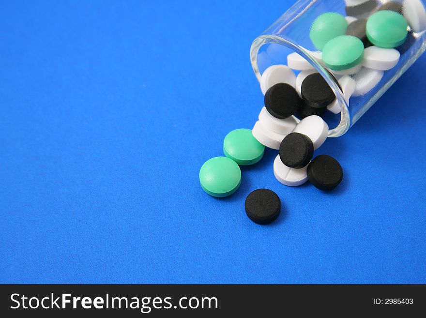 Green, white and black pills in the glass cup on a blue background