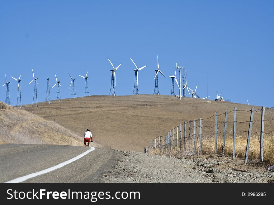 A lone cyclist with wind turbine on background. A lone cyclist with wind turbine on background