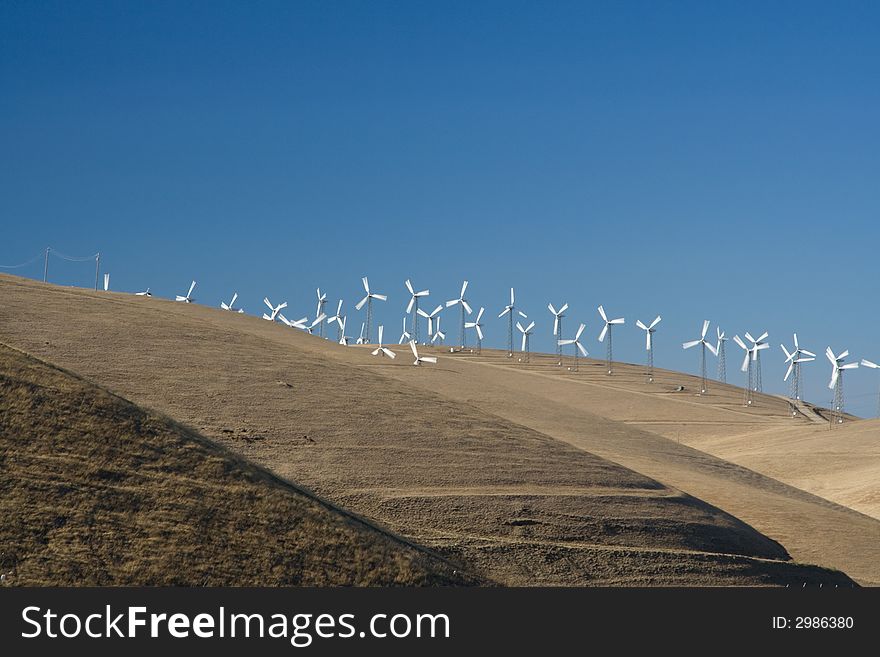 Windfarm turbines on yellow grassed hills with blue cloudless skys. Windfarm turbines on yellow grassed hills with blue cloudless skys.