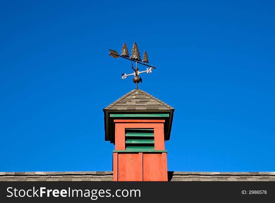 A view of a red cupola and weather vane on top of a barn on a sunny, cloudless summer day. A view of a red cupola and weather vane on top of a barn on a sunny, cloudless summer day.