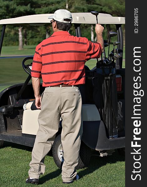 Male golfer picks driver club from golf bag on back of cart. Male golfer picks driver club from golf bag on back of cart.