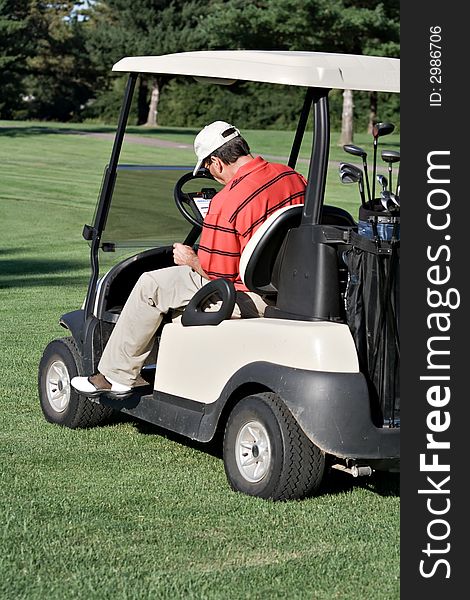 Male golfer sits in cart records his score on score card. Male golfer sits in cart records his score on score card.