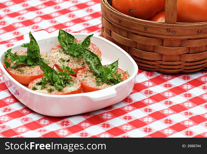 A baking dish with tomatoes prepared to be baked with basil, parsley.  Basket of fresh tomatoes. A baking dish with tomatoes prepared to be baked with basil, parsley.  Basket of fresh tomatoes.