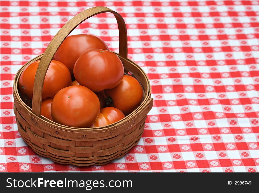 A wooden woven basket of fresh garden tomatoes on tablecloth. A wooden woven basket of fresh garden tomatoes on tablecloth.