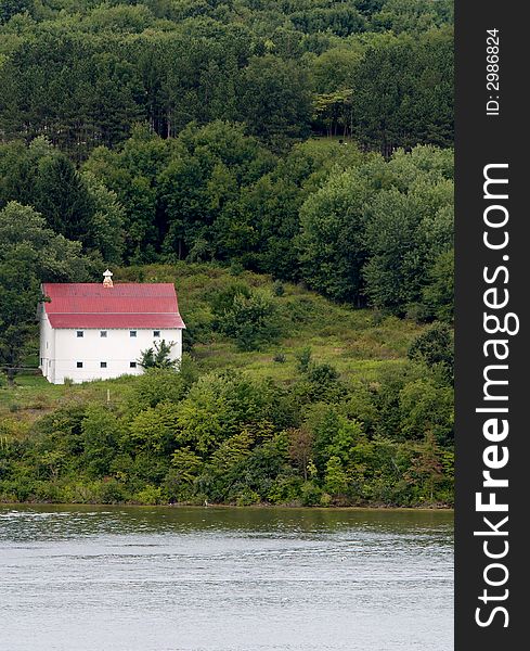 An old barn on a hill near a lake.