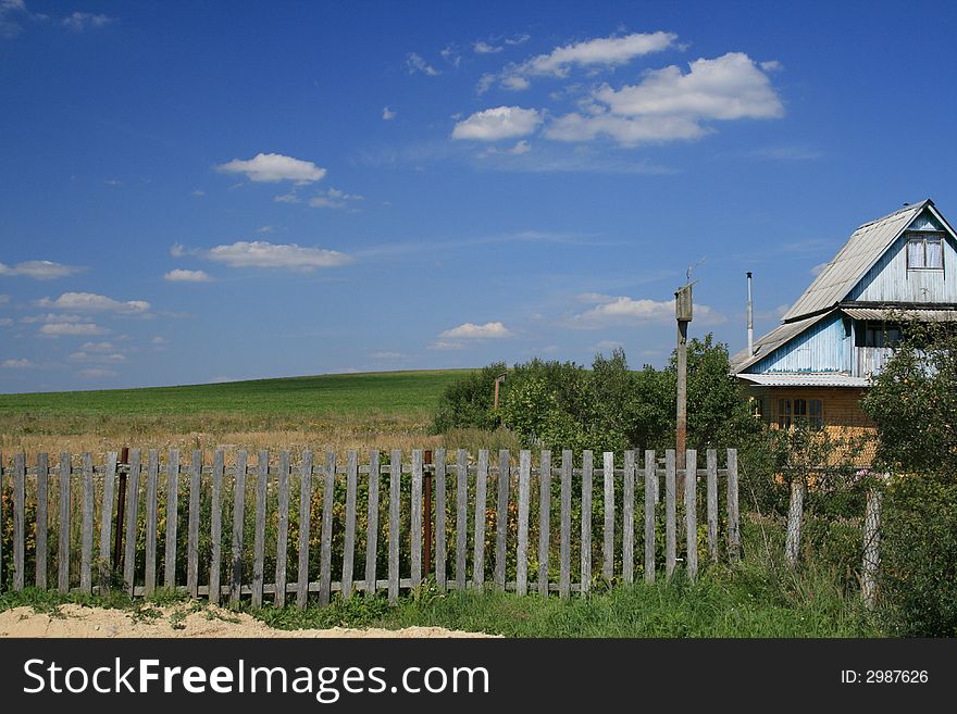 The village house and the green field landscape and blue sky with clouds as a background.