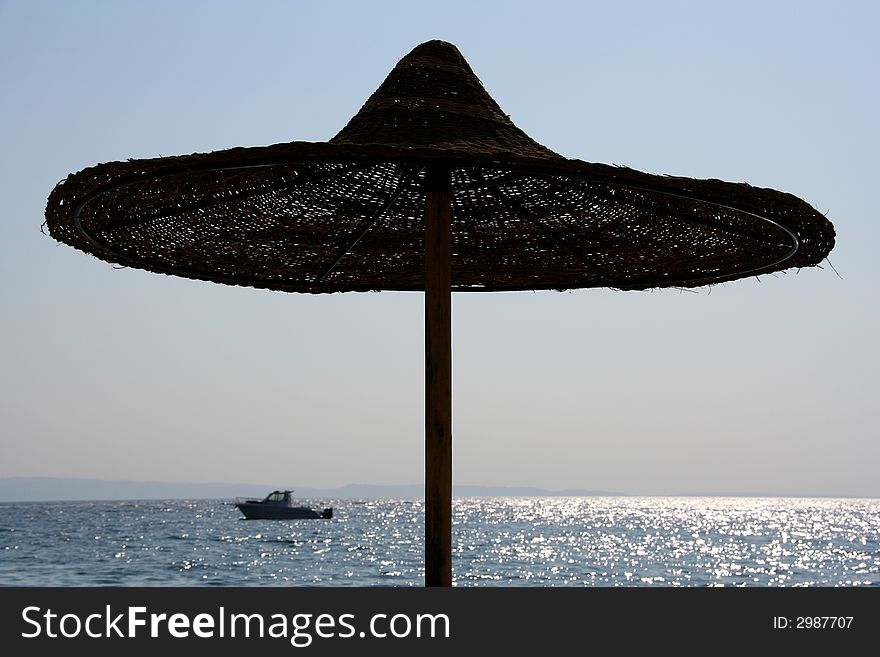 The silhouette of a beach parasol against the sparkling sea. The silhouette of a beach parasol against the sparkling sea