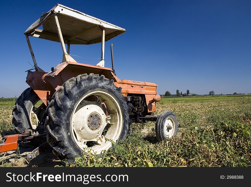 An old orange farm tractor in a cultivated land in countryside. An old orange farm tractor in a cultivated land in countryside