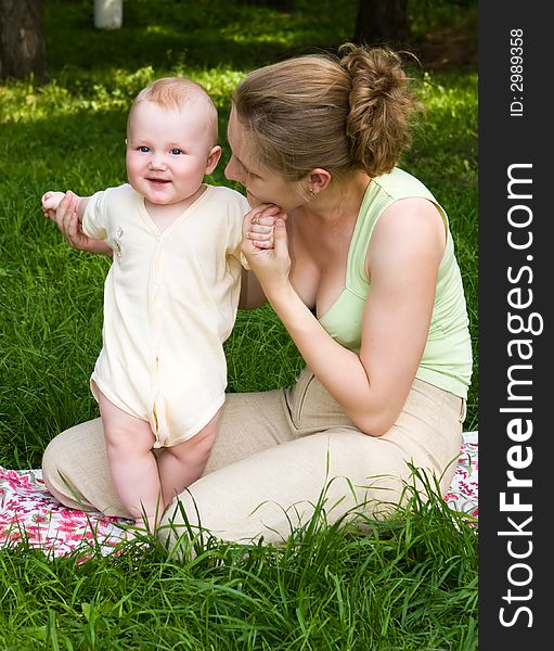 Mother supports the child stand on a green grass. Mother supports the child stand on a green grass