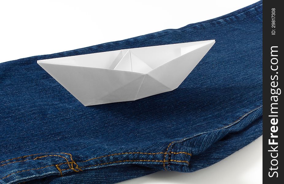 A paper boat sailing on a blue stream made of a pair of blue jeans. A paper boat sailing on a blue stream made of a pair of blue jeans