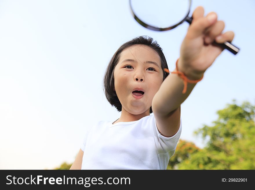 Asian little girl holding a magnifying glass in outdoor