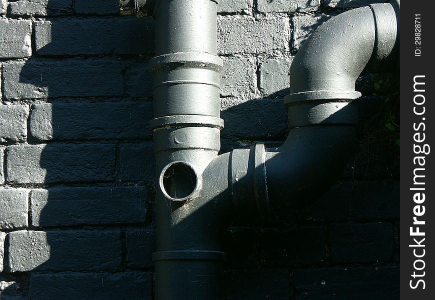 Grey painted sewage pipes against grey painted brick wall lit by direct sunlight. Grey painted sewage pipes against grey painted brick wall lit by direct sunlight