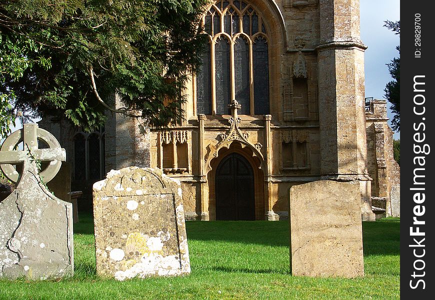 West wall of medieval church seen through trees and tombstones of churchyard