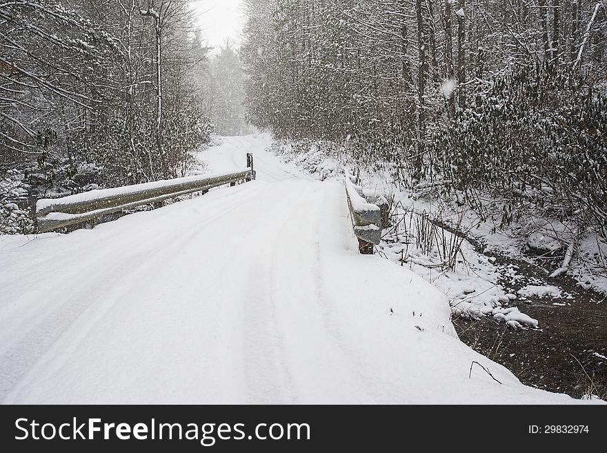 Snow covers a narrow mountain bridge.