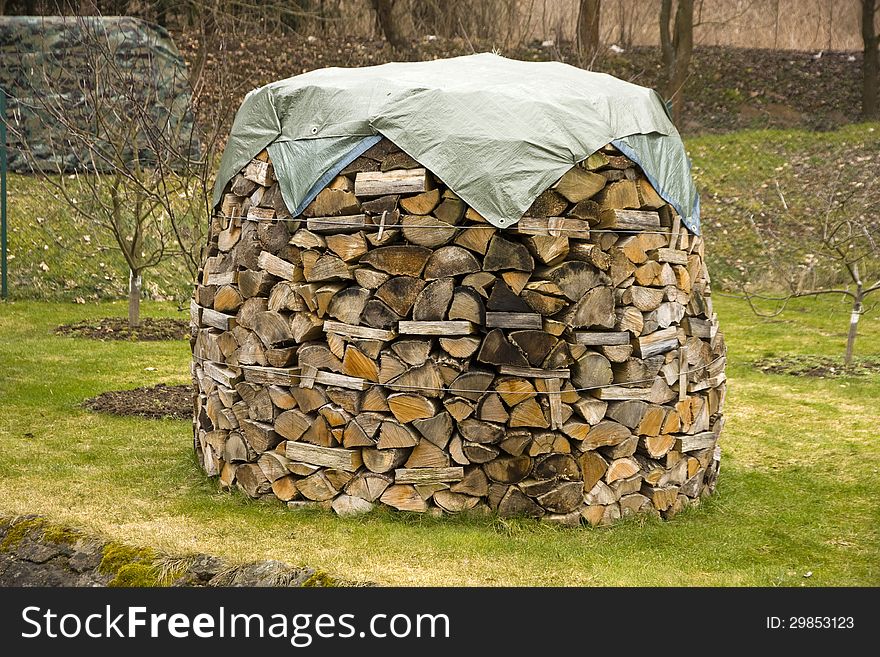 Chopped wood piled round mast, pile of wood covered with a tarpaulin. Chopped wood piled round mast, pile of wood covered with a tarpaulin