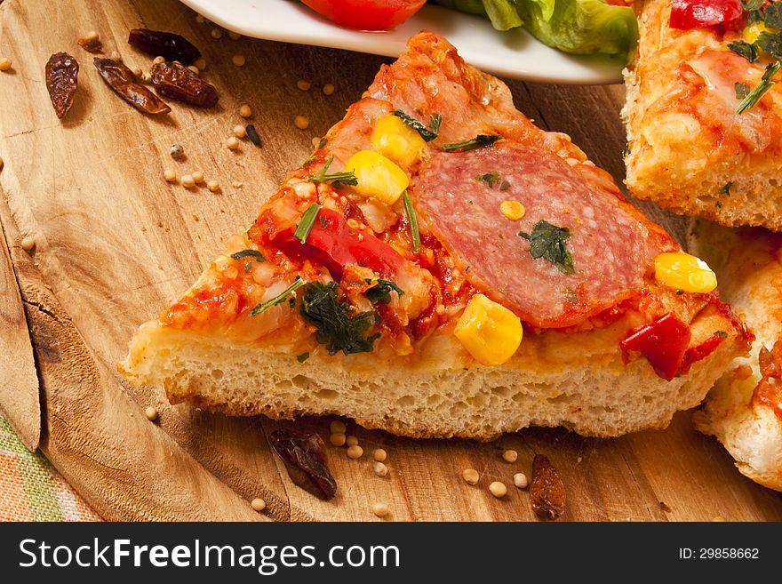 Slice of salami pizza sitting on wooden cutting board